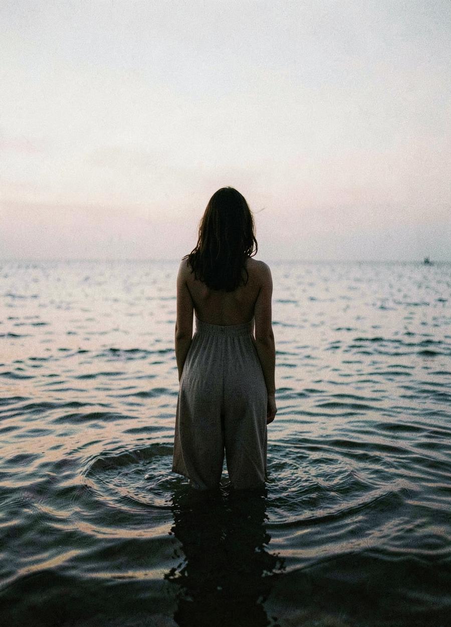 Woman standing in shallow sea water at dusk